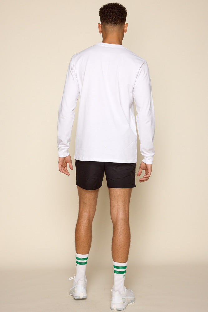 Full back view of male model wearing a long sleeve shirt along with black shorts white socks with green stripes and white sneakers