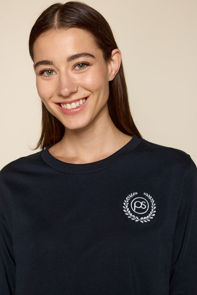 Close up photo of female model wearing long sleeve tee with white graphic of "PS" surrounded by victory wreath