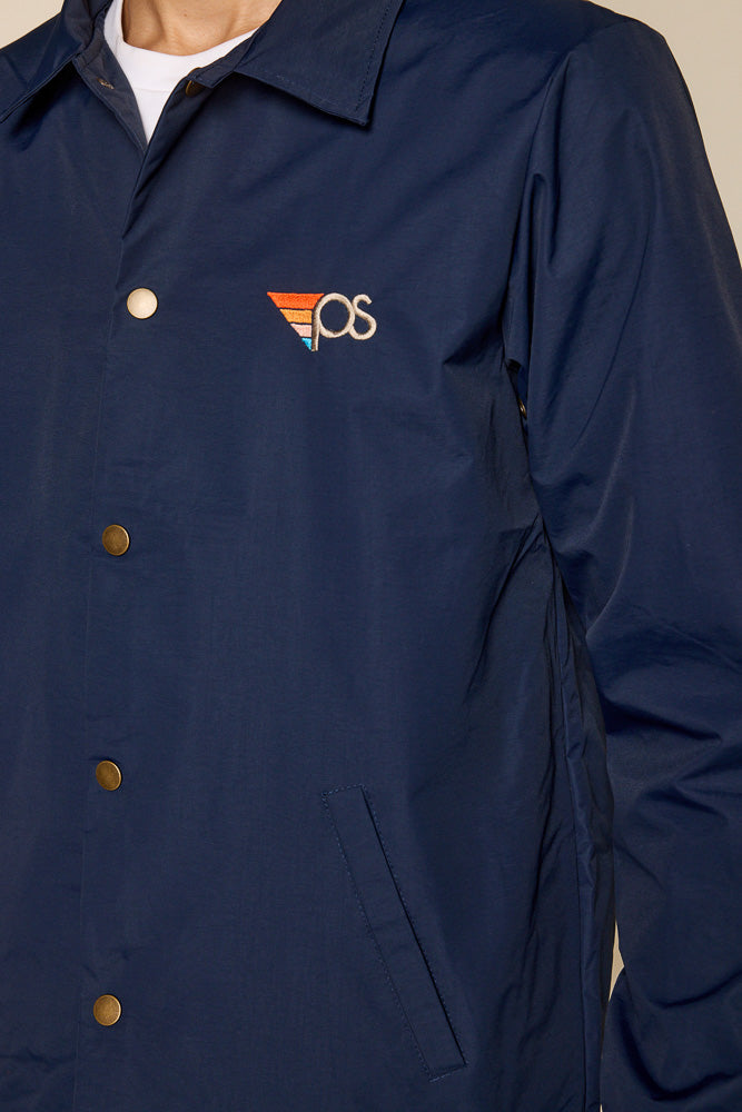 Close up photo of water resistant navy jacket. Can see detail of the snap on buttons and graphic on the upper left side. "PS"