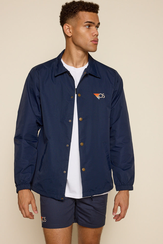 Cropped photo of male model wearing navy snap on water resistant coach jacket. Graphic on the upper left chest is a "PS" embroidered