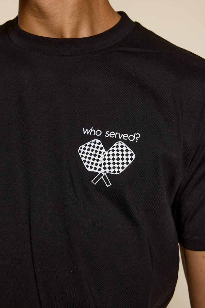 Cropped photo of male model wearing a black tee with graphic on the upper left chest in white of two crisscrossed pickleball checkered paddles under the font saying "who served?"