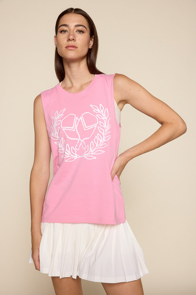 Female model wearing a pink muscle shirt top and a white pleated skirt. The top has a graphic of crisscross paddles and victory wreath surrounding it.