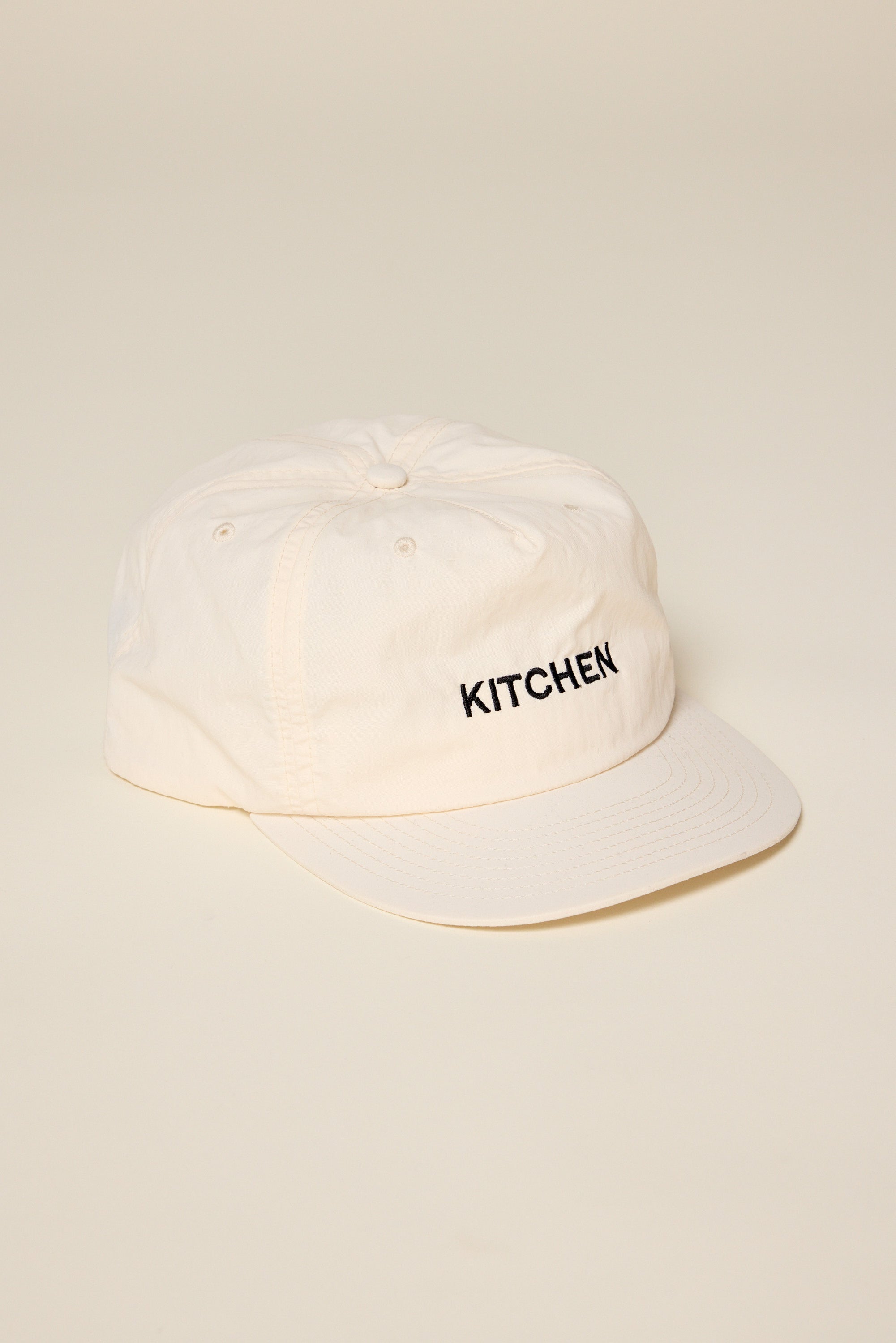 Beige hat embroided with the word Kitchen. the emboidery color is black