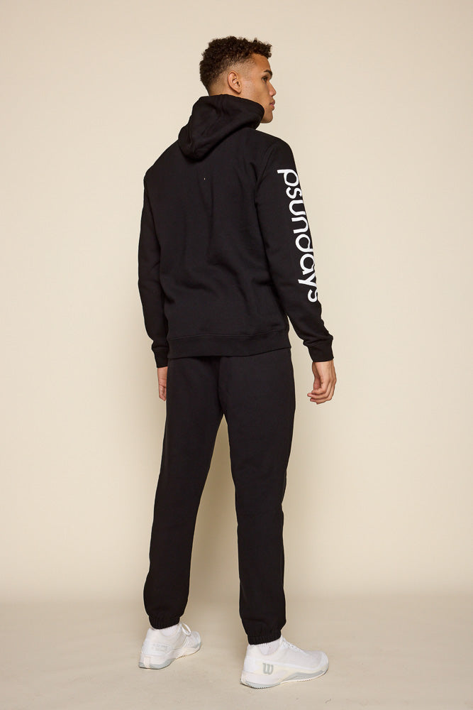 Full back view of male model sporting black hoodie with Psunday logo in white print. Model is also wearing a black jogger and white sneakers